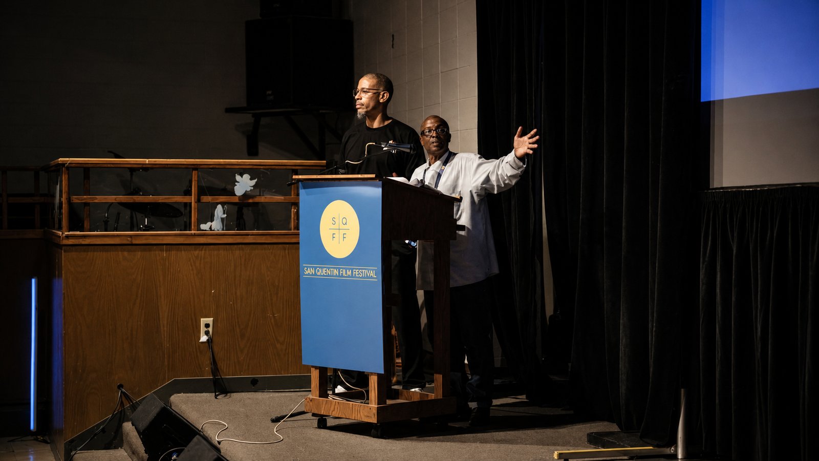 Two men address the audience from the festival podium